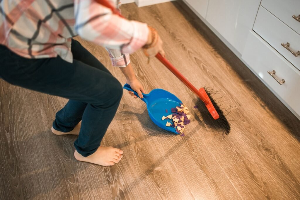 Persona barriendo restos del piso con escoba y recogedor
